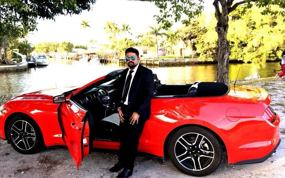 Man in suit by red Mustang convertible at waterfront
