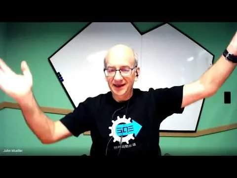 Video-call frame captioned John Mueller, arms raised, SOE T-shirt