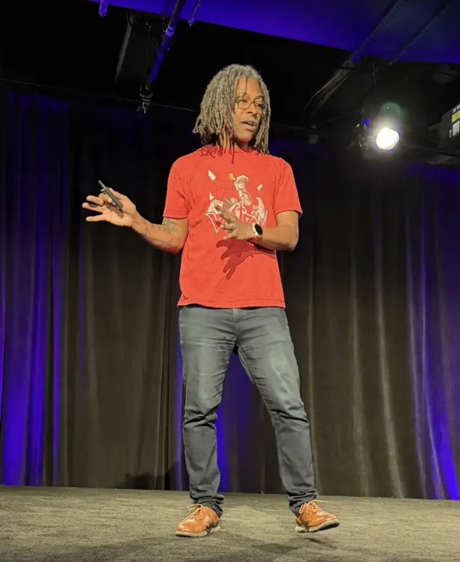 Speaker with long locs in red T-shirt presenting on stage